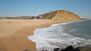 Een strand met een hoge klif, heldere lucht en een paar gebouwen op de achtergrond.