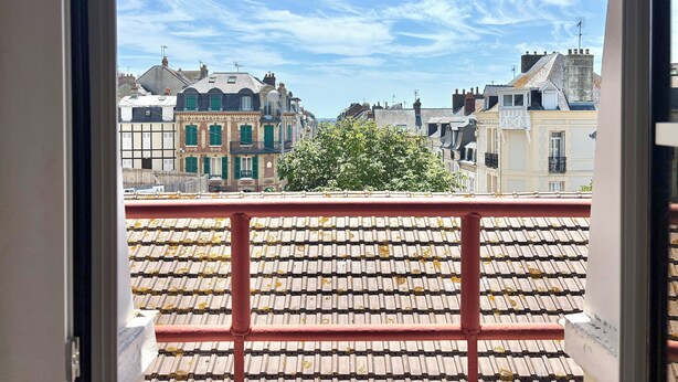 A view from a balcony with a tiled floor, overlooking a row of buildings with varied architecture and a clear sky. - Family home close to the beach and town centre (Trouville-sur-Mer)