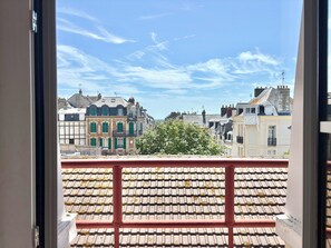 En utsikt från en balkong med ett klinkergolv, med utsikt över en rad byggnader med varierande arkitektur och en klar himmel.