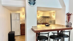 A kitchen with a clock, a refrigerator, a microwave, a sink, and a bar area with stools. - Family home close to the beach and town centre (Trouville-sur-Mer)