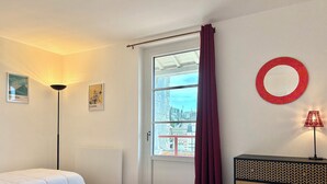 A hotel room with two beds, a window with curtains, a wall-mounted mirror, and a lamp. - Family home close to the beach and town centre (Trouville-sur-Mer)