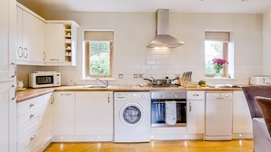 A modern kitchen with white cabinetry, a microwave, a stove, a washing machine, and a dishwasher. - 3 Bed in Wareham (oc-dc157) (Stoborough)
