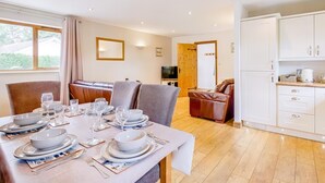 A dining area with a table set for four, a sofa, a television, and a kitchen area with cabinets. - 3 Bed in Wareham (oc-dc157) (Stoborough)