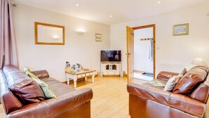 A living room with two brown leather sofas, a wooden coffee table, a television, and a door leading to a bathroom. - 3 Bed in Wareham (oc-dc157) (Stoborough)