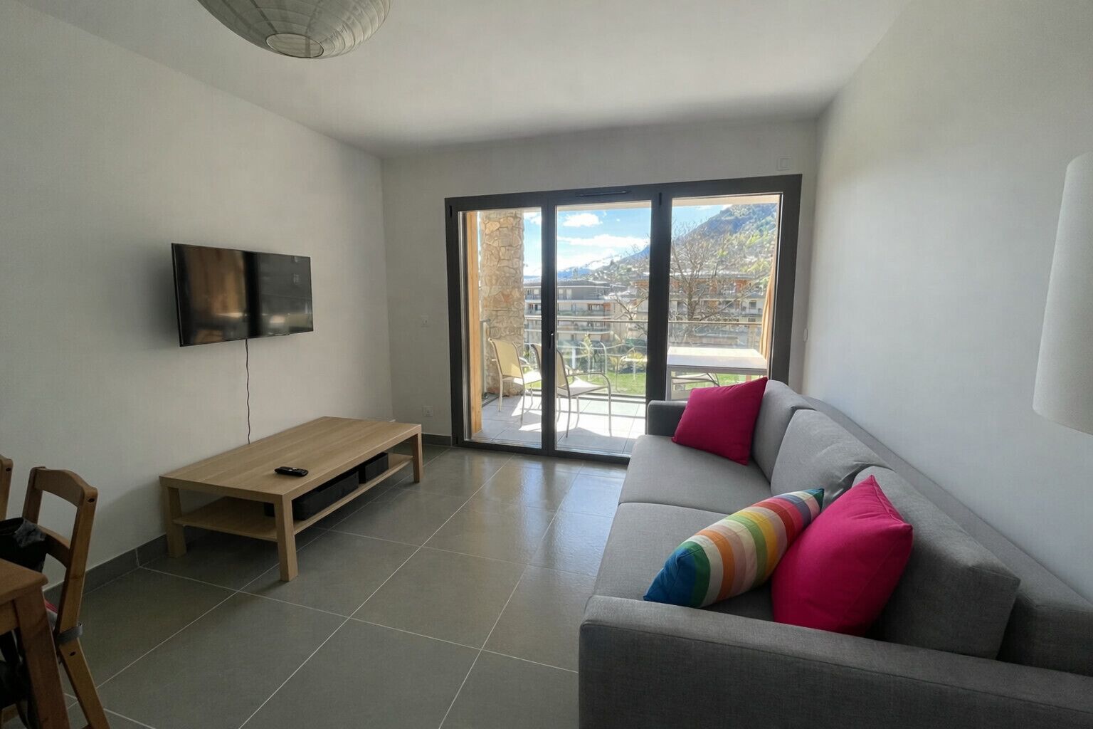 A modern living room with a grey sofa, colorful pillows, a wooden coffee table, and a TV mounted on the wall.
