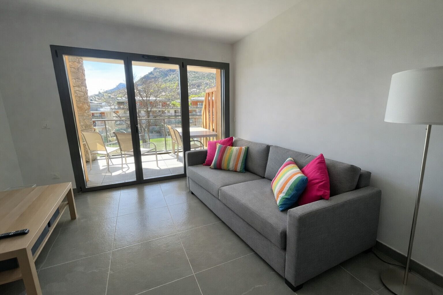 A modern living room with a grey sofa, colorful pillows, a wooden table, and a floor lamp.