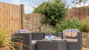 Eine Terrasse mit Korbmöbeln, einem Tisch mit Teekanne und einem Blumentopf.