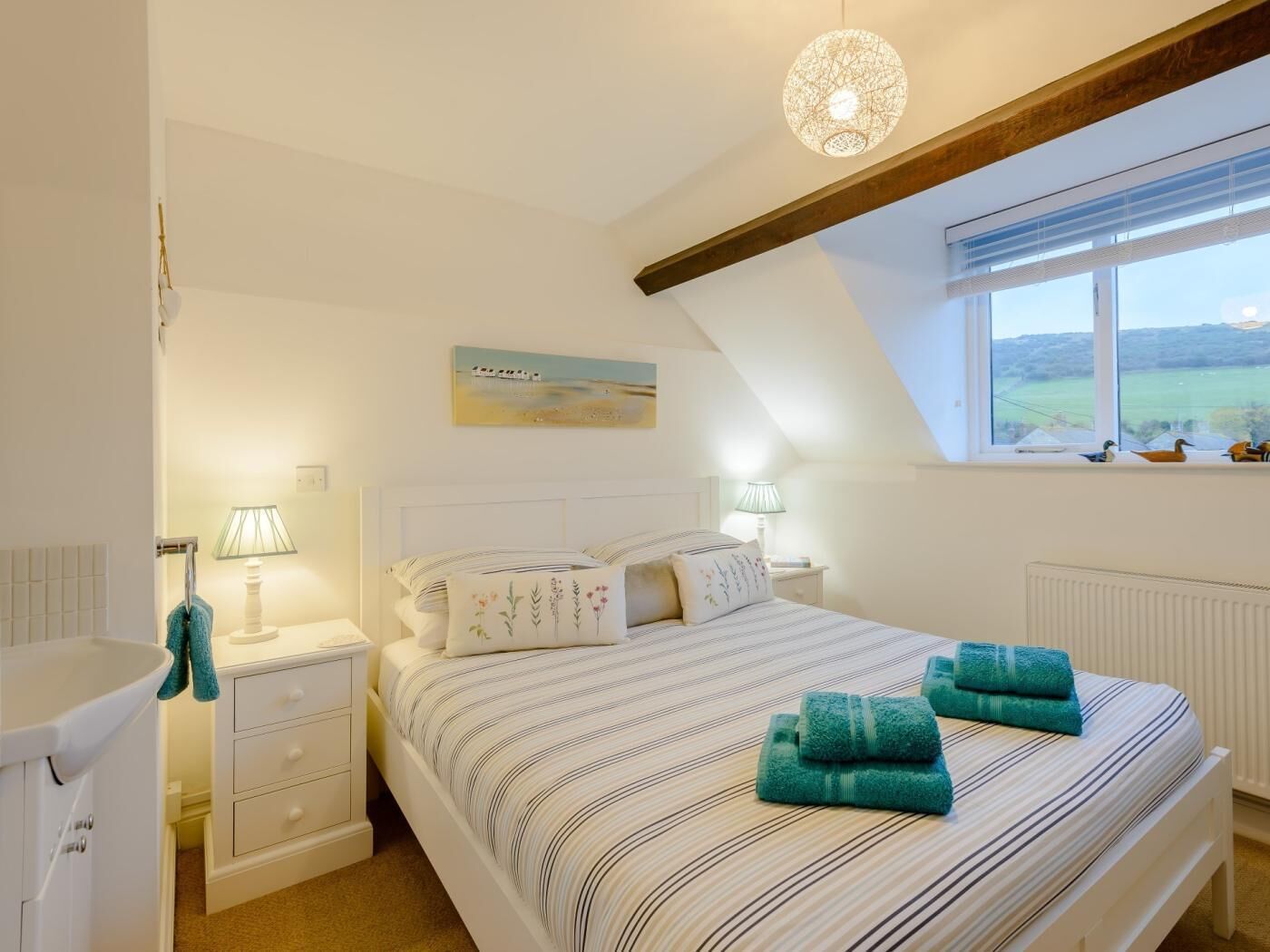 Une chambre à coucher avec un lit, des tables de chevet, une fenêtre donnant sur un beau paysage et un tableau accroché au mur.