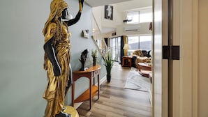 Eine Statue in einer Halle mit einer Treppe, einem Blumentopf und Blick auf ein Wohnzimmer mit einer Couch und einer Lampe.