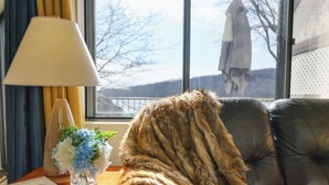 Ein Zimmer mit Fenster, Lampe, Blumen in einer Vase und einem fellüberzogenen Gegenstand.