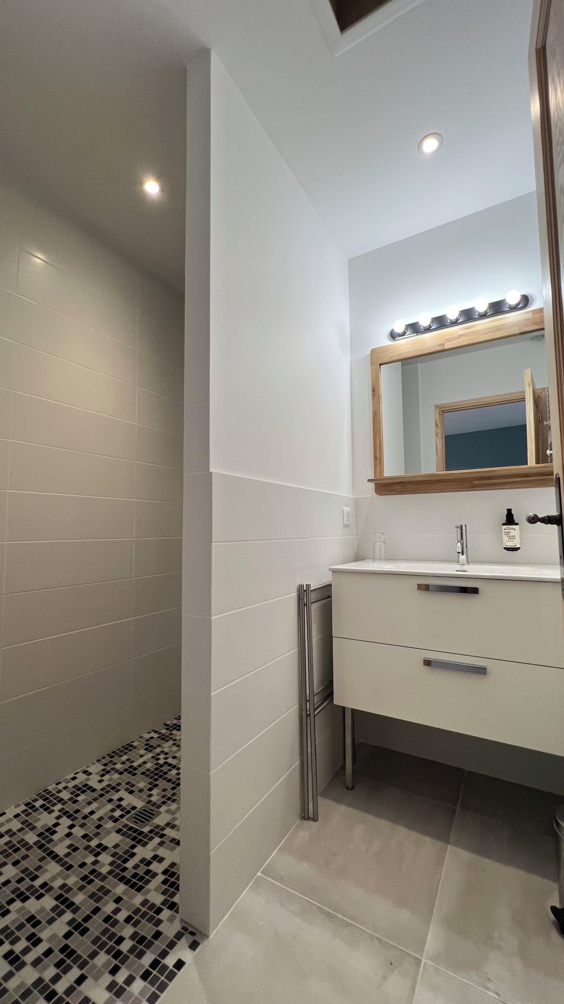 Een badkamer met een douche, een wastafel met spiegel en een betegelde vloer.