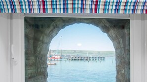 Blick durch einen steinernen Bogen auf ein Gewässer, einen Kran und einen Pier in der Ferne.
