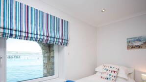 Ein Schlafzimmer mit Bett, einem Fenster mit Meerblick und einem Gemälde an der Wand.