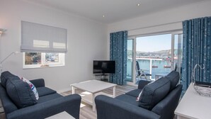 Ein modernes Wohnzimmer mit Fernseher, zwei Sofas, einem Couchtisch und einem großen Fenster mit Vorhängen.