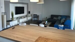 Uma sala de estar moderna com uma ilha central, uma televisão de tela plana na parede e um sofá com almofadas.
