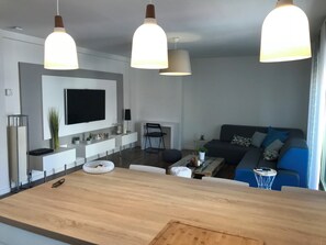 A modern living room with a central island, a flat-screen TV mounted on the wall, and a sofa with cushions. - Bright apartment near center and beaches (Cannes)