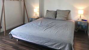 Quarto com cama, duas mesas de cabeceira com luminárias, uma escada de madeira e um varal fixado na parede.