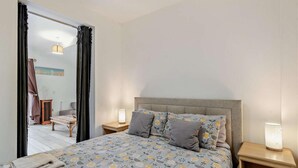 A bedroom with a bed, two bedside tables, a nightstand, a window with curtains, a radiator, and a view of the outside. - 2 Bed in Mablethorpe (oc-74809) (Mablethorpe and Sutton)