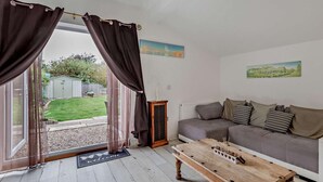 A living room with a grey sofa, a wooden coffee table, and a view of a garden through a glass door. - 2 Bed in Mablethorpe (oc-74809) (Mablethorpe and Sutton)