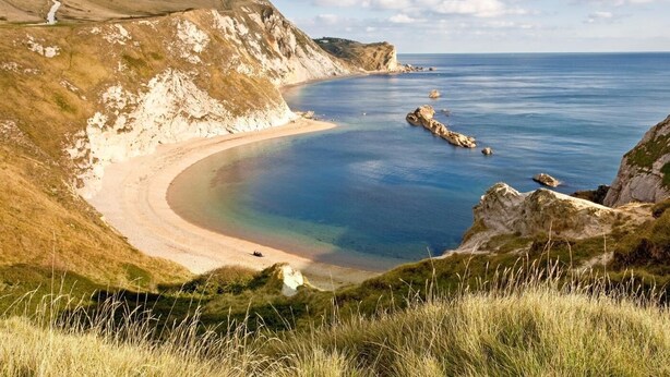 A coastal landscape with cliffs, a beach, and clear blue water.