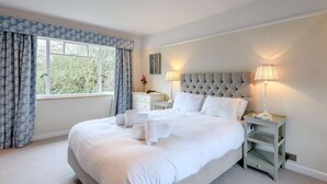 A bedroom with a large bed, two bedside tables, a nightstand, a window with curtains, and a lamp.