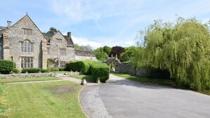A stone building with a paved driveway, a stone bridge, and lush greenery.