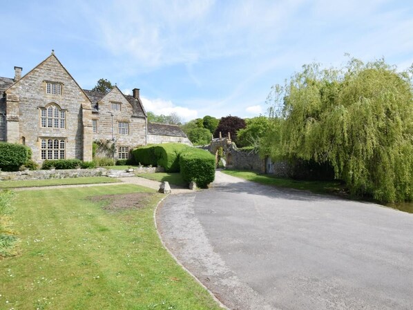 A stone building with a paved driveway, a stone bridge, and lush greenery.