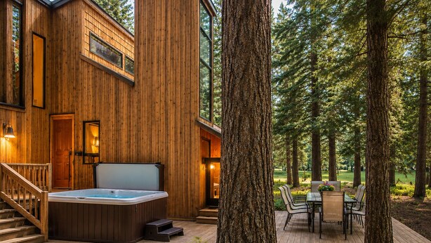 Una baita di legno con idromassaggio, posti a sedere all'aperto e una terrazza circondata da alberi.