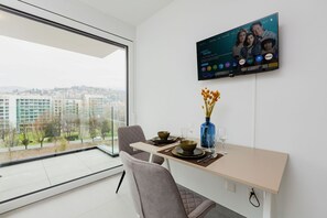 A modern dining area with a large window, a flat-screen TV mounted on the wall, and a vase with flowers on the table. - {Suite 404} Gym, Business Room, Modern, Relax (Lugano)