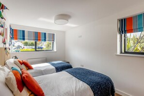 A bedroom with two beds, a radiator, and windows with striped curtains. - 4 Bed in Bideford (oc-75358) (Northam)