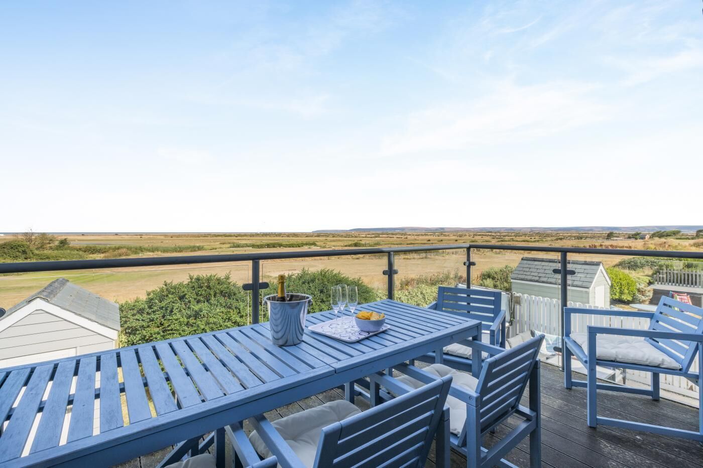 A balcony with a table and chairs, a bottle of champagne, and a view of the countryside.