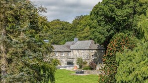 A stone building with a lawn in front, surrounded by trees. - 12 Bed in Bala (oc-75289) (Llandderfel)