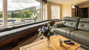 A living room with a view of a lake and hills, a sofa, a bench, and a coffee table with a vase of flowers. - 12 Bed in Bala (oc-75289) (Llandderfel)
