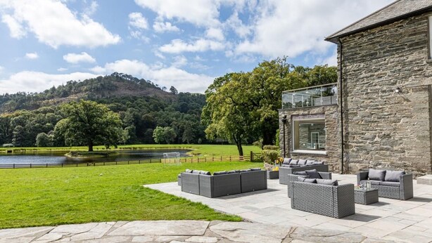 A stone building with a patio area featuring outdoor furniture and a view of a lake and hills. - 12 Bed in Bala (oc-75289) (Llandderfel)