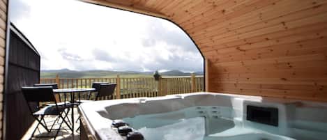 Una terraza de madera con un jacuzzi y mobiliario exterior.