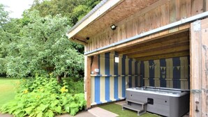 Een houten gebouw met een overdekt terras, een jacuzzi en een kleine opstap.'