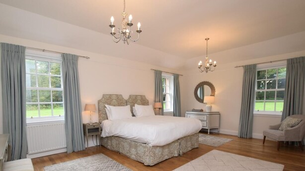 Een slaapkamer met een groot bed, twee nachtkastjes, een stoel, een spiegel en een kroonluchter.