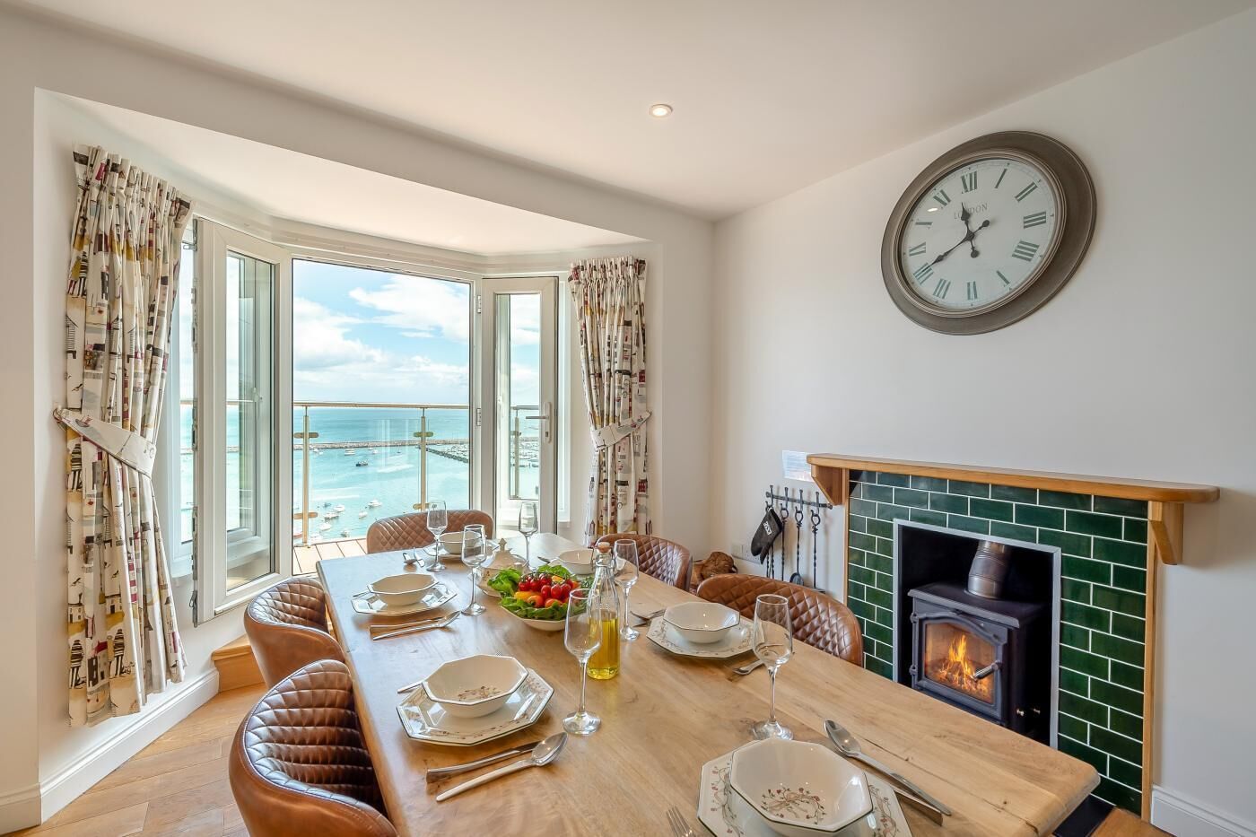 A dining room with a view of the sea, a fireplace, and a clock on the wall.