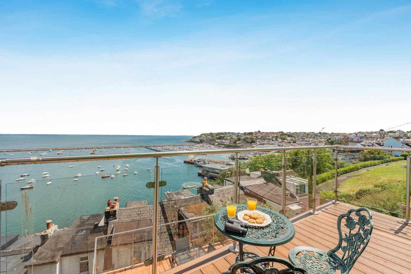 A balcony with a table, chairs, and a view of the sea and town.