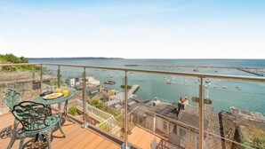 Ein Balkon mit Blick auf einen Yachthafen, ein Tisch mit einem Stuhl und eine stehende Person.