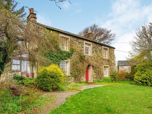 A stone house with a red door, surrounded by greenery and a gravel path. - 4 Bed in Penrith (oc-sz054) (Matterdale End)