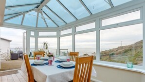 Ein Wintergarten mit Esstisch, großen Fenstern und Blick auf die Landschaft.