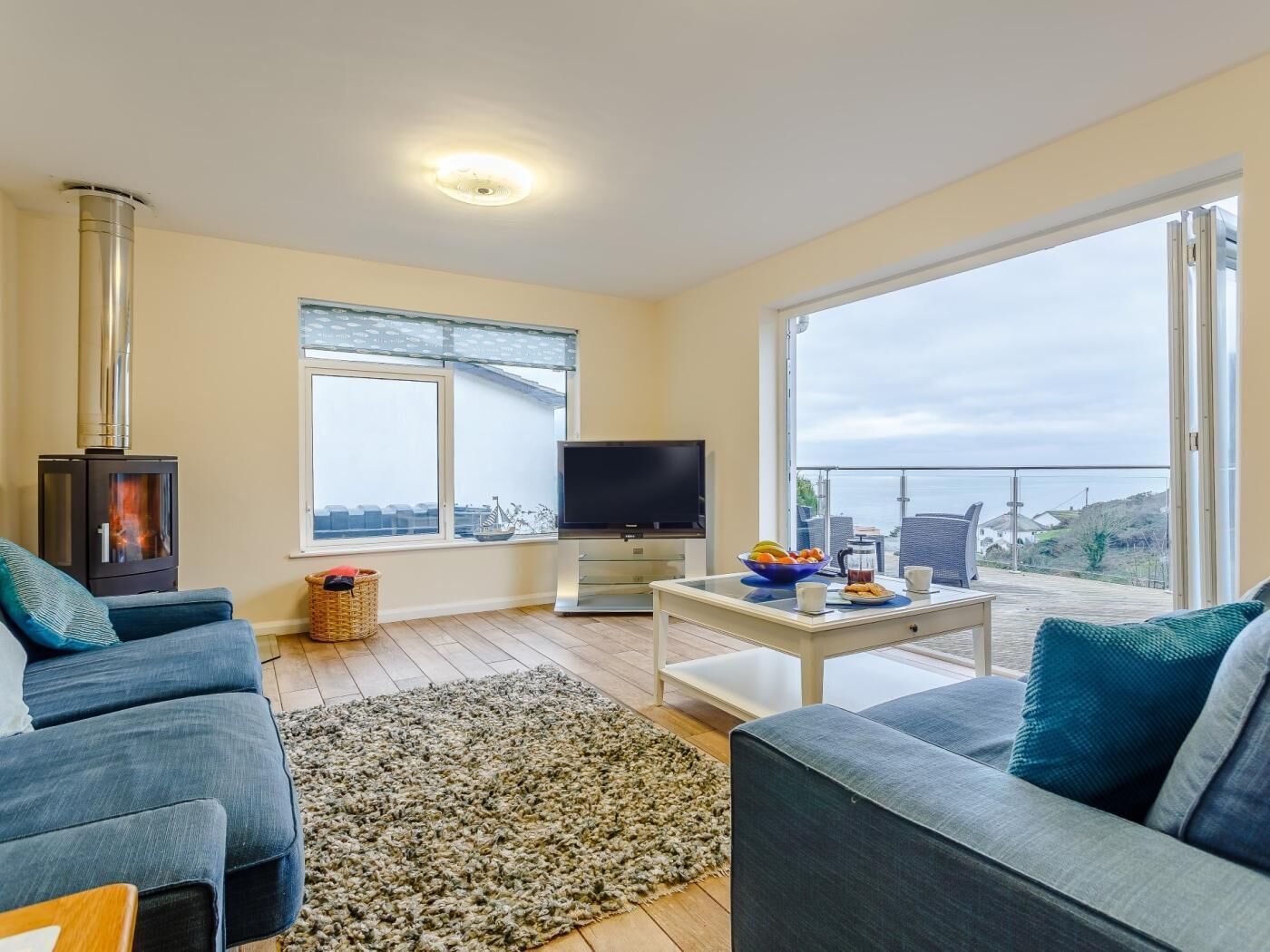 A living room with a sofa, a television, a table with a bowl and cups, a fireplace, and a balcony with a view.