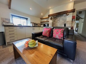 Eine moderne Küche mit Steinrückwand, ein schwarzes Ledersofa mit roten Kissen und ein Holztisch mit Obst.