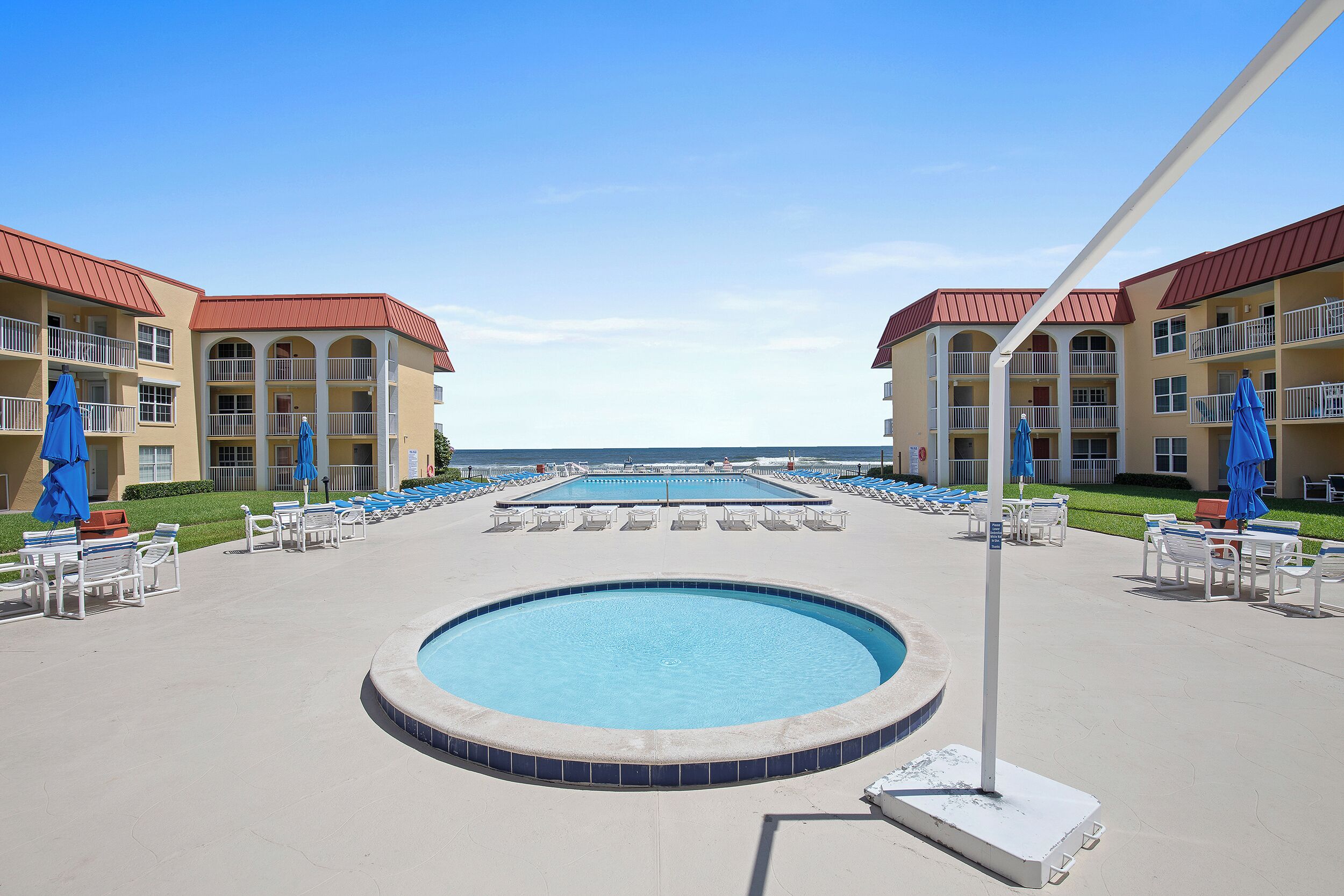 A pool area with lounge chairs and umbrellas, surrounded by multi-story buildings with balconies.