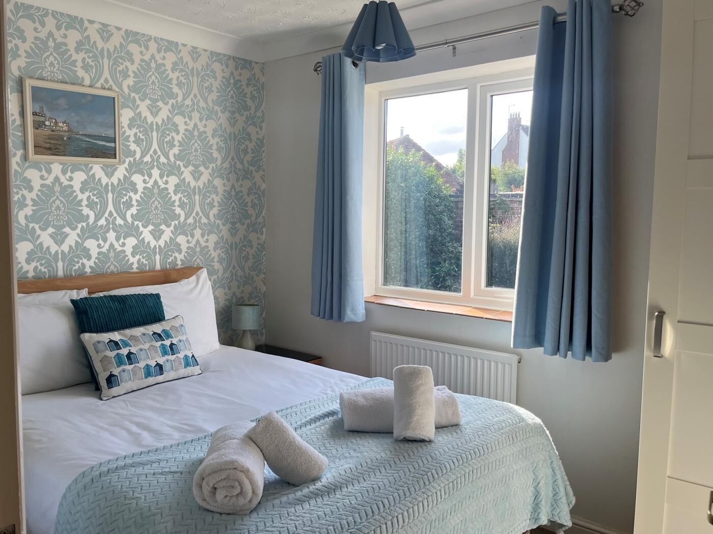 Un dormitorio con cama, ventana con cortinas, radiador y papel tapiz estampado en la pared.