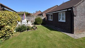 A residential property with a well-maintained lawn, a patio with outdoor furniture, and a brick house with a tiled roof. - 2 Bed in Norwich (oc-75398) (Mundesley)
