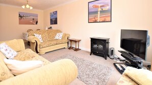 A living room with a sofa, a television, a fireplace, and wall art. - 2 Bed in Norwich (oc-75398) (Mundesley)