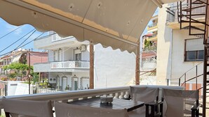 En uteplats med ett bord och stolar, ett takförsett område och utsikt över bostadshus.