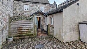 Ein Steinhaus mit einem Holztor, einem Kopfsteinpflasterhof und einer kleinen Tür mit der Aufschrift 'COTTAGE'.